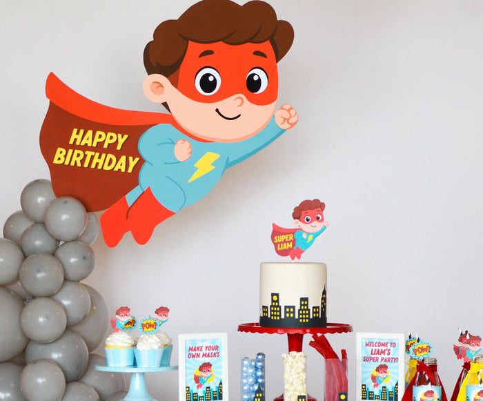Superhero birthday party dessert table with comic-book banner, personalized cake topper, and Hero Fuel snack signs