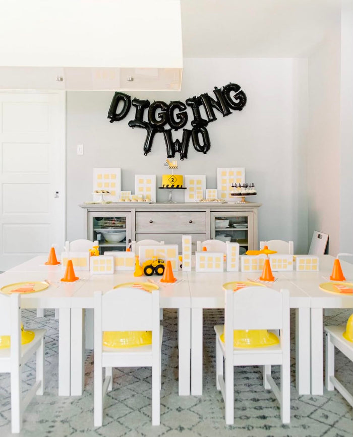 Construction birthday party tablescape with a DIGGING TWO balloon banner, dessert table, and kids' seating with traffic cones and hard hats