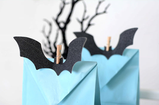 Glitter Bat Halloween Gift Tags close-up of black glitter bat clips on light blue kraft favor bags with black branch decor in background